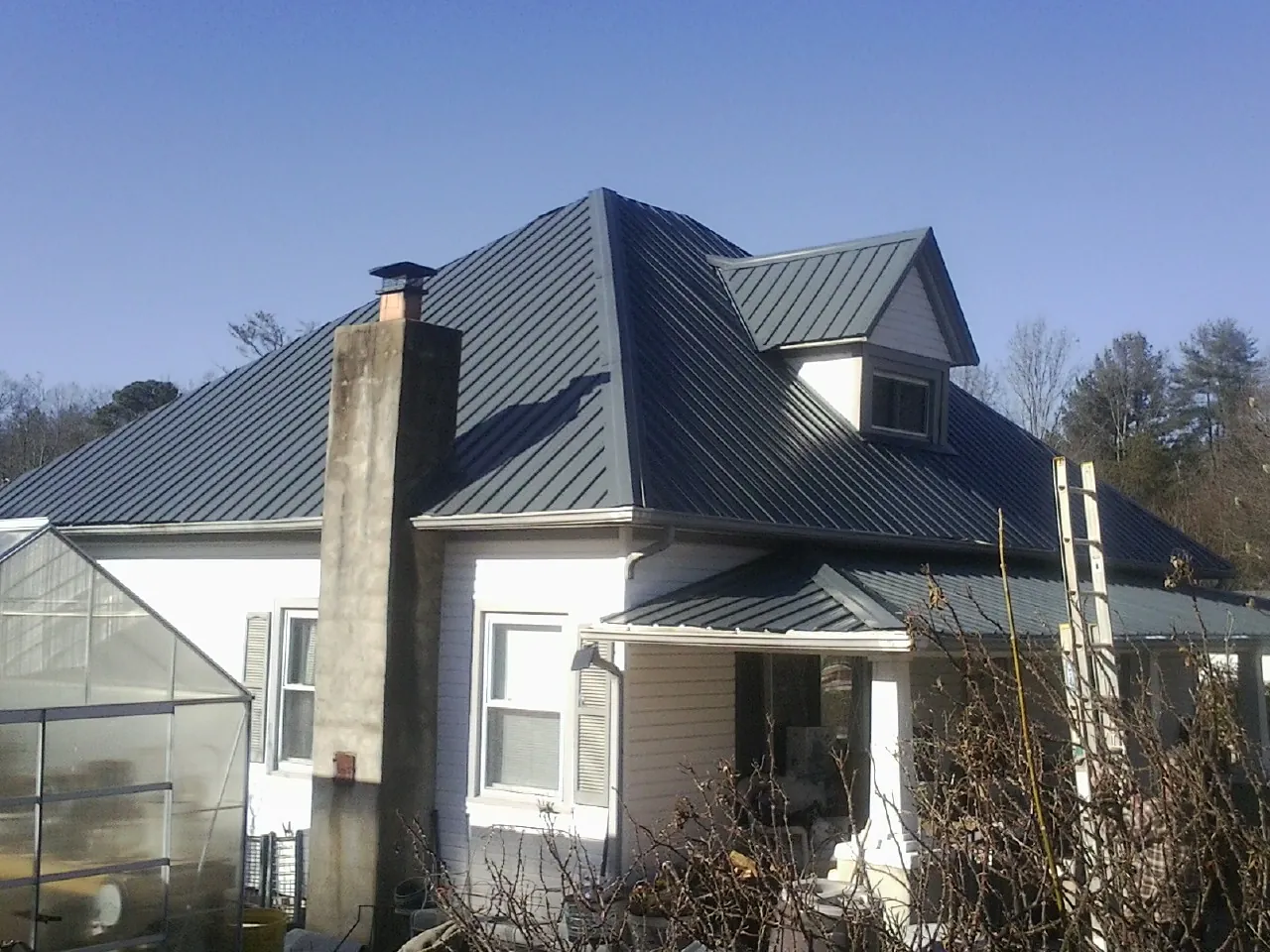 Dark blue standing seam metal roof on a white farmhouse with dormer — Slate & Tile Roof Repair by Roofing Brothers in Indian Lake Estates