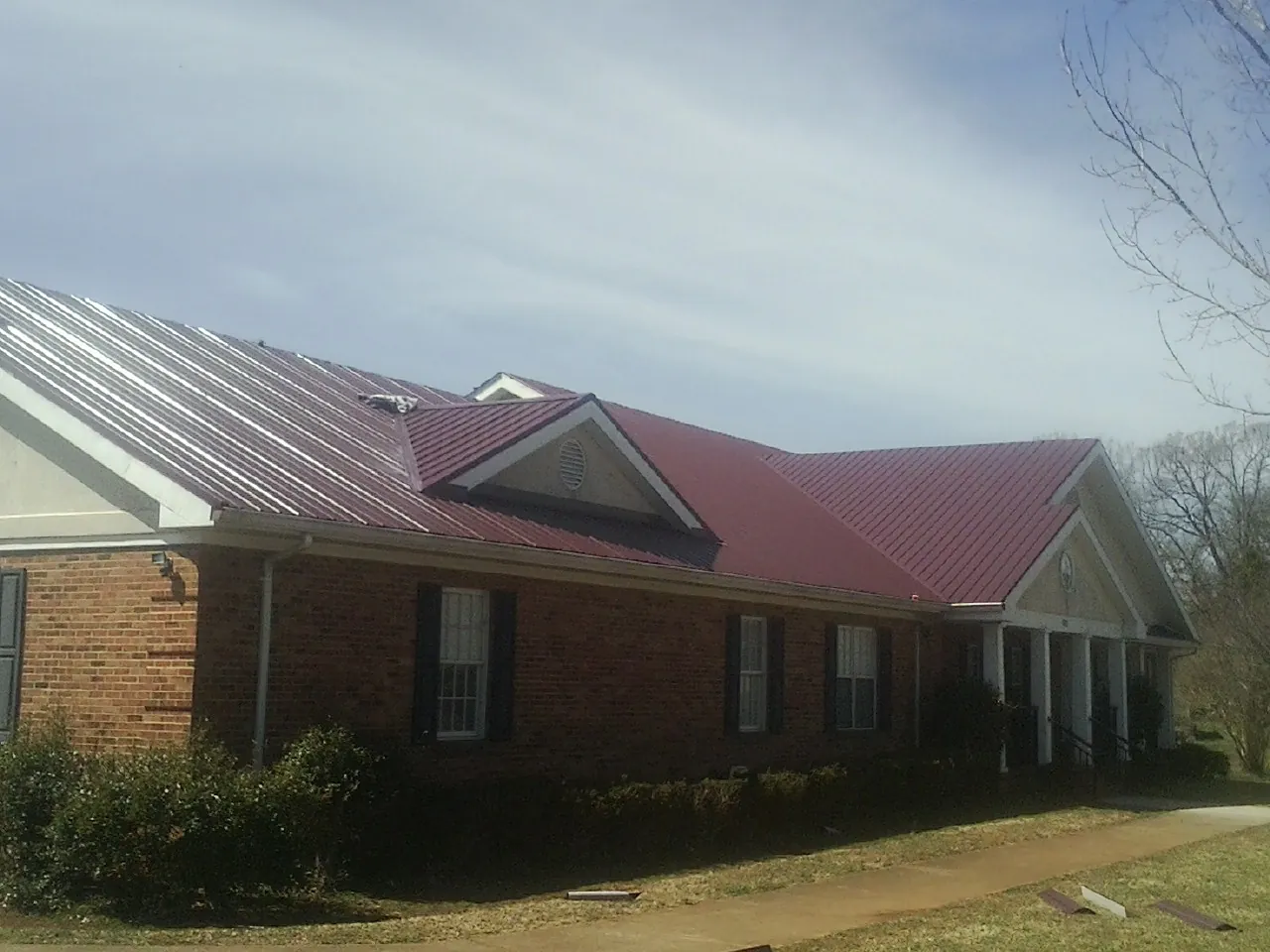 Red metal roof with gabled entries on a long brick building, from a Hail Damage Roof Repair job in Indian Lake Estates