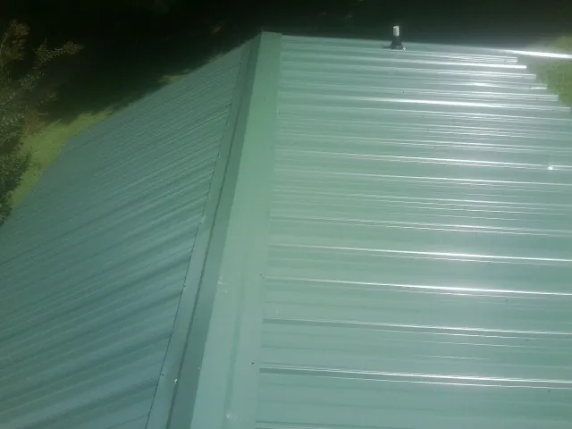 New green metal panels meeting at the ridge of a roof — Flat Roof Repair work by our crew in Indian Lake Estates