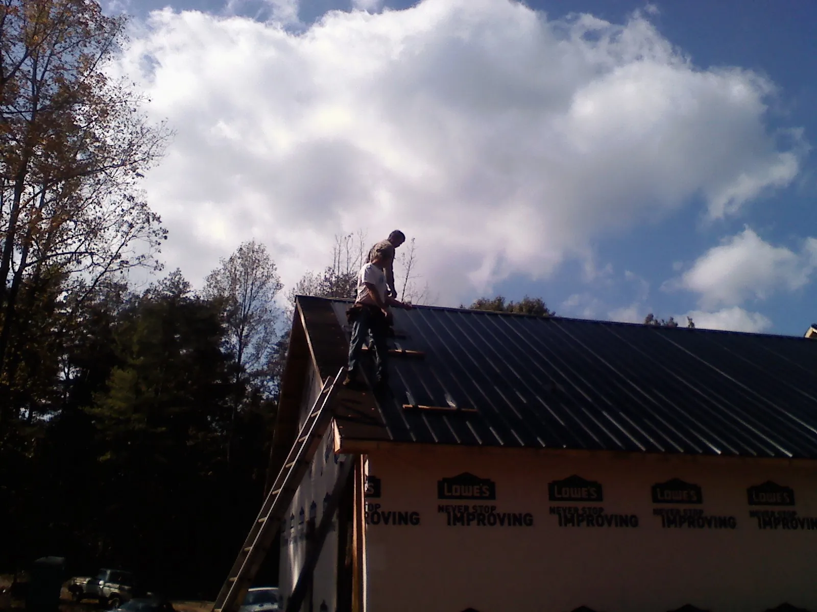 Roofer fastening dark metal panels high against a cloudy sky, from a Roof Inspection job in Indian Lake Estates