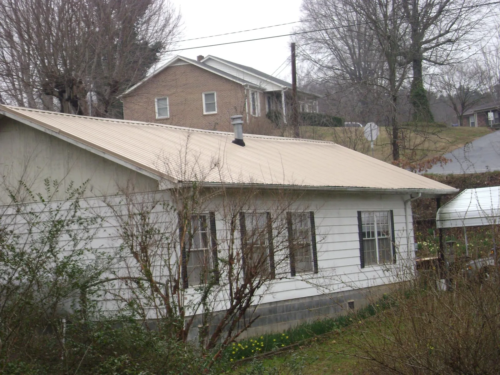 Tan metal roof on a white sided house set into a hillside — Commercial Roofing by Roofing Brothers in Indian Lake Estates