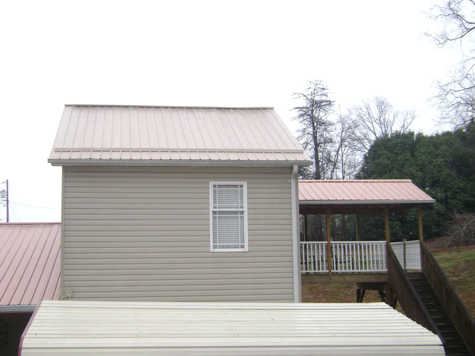 Tan metal roofs on a two story addition and attached porch, from a Roof Replacement job in Indian Lake Estates